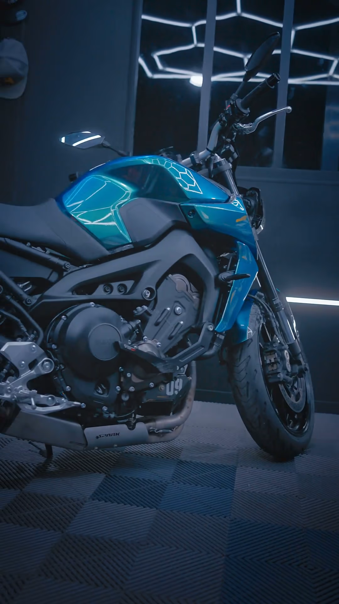 Moto turquoise sous les néons hexagonaux d’un atelier — Le Labo d’Amad
