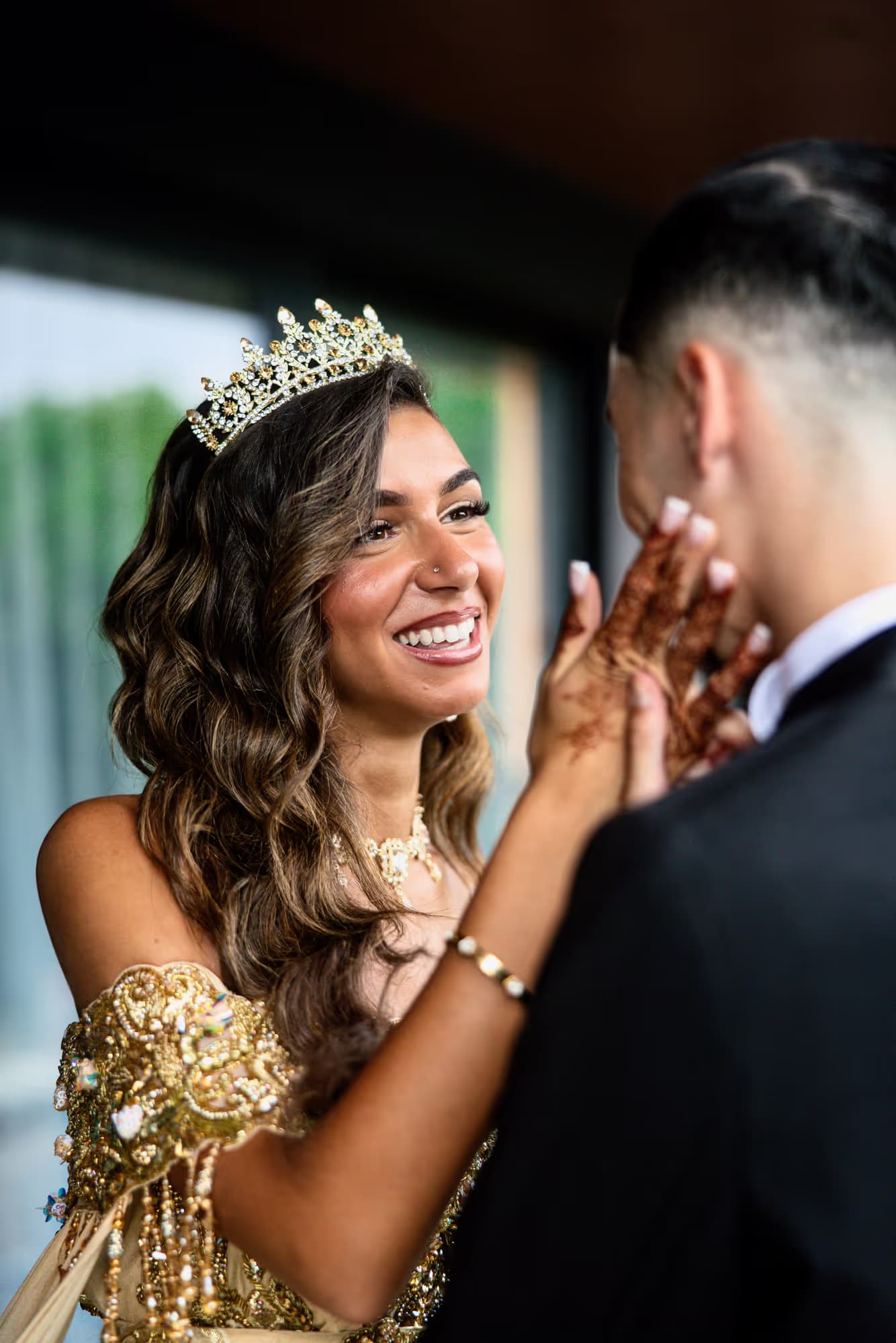 La mariée souriante en diadème, main au henné posée sur la joue du marié